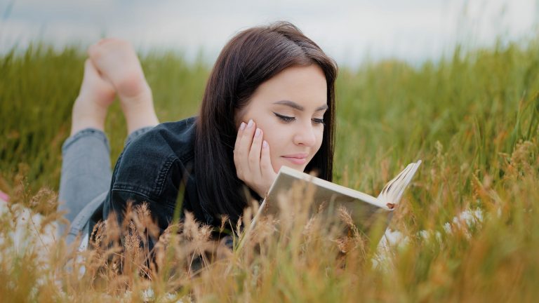 Young attractive brunette caucasian woman girl lying on grass pretty teenage girlfriend student read